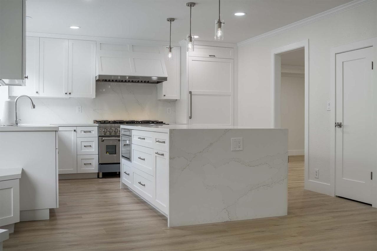 Luxury home remodeling kitchen featuring pendant lighting over quartz island with white cabinetry throughout