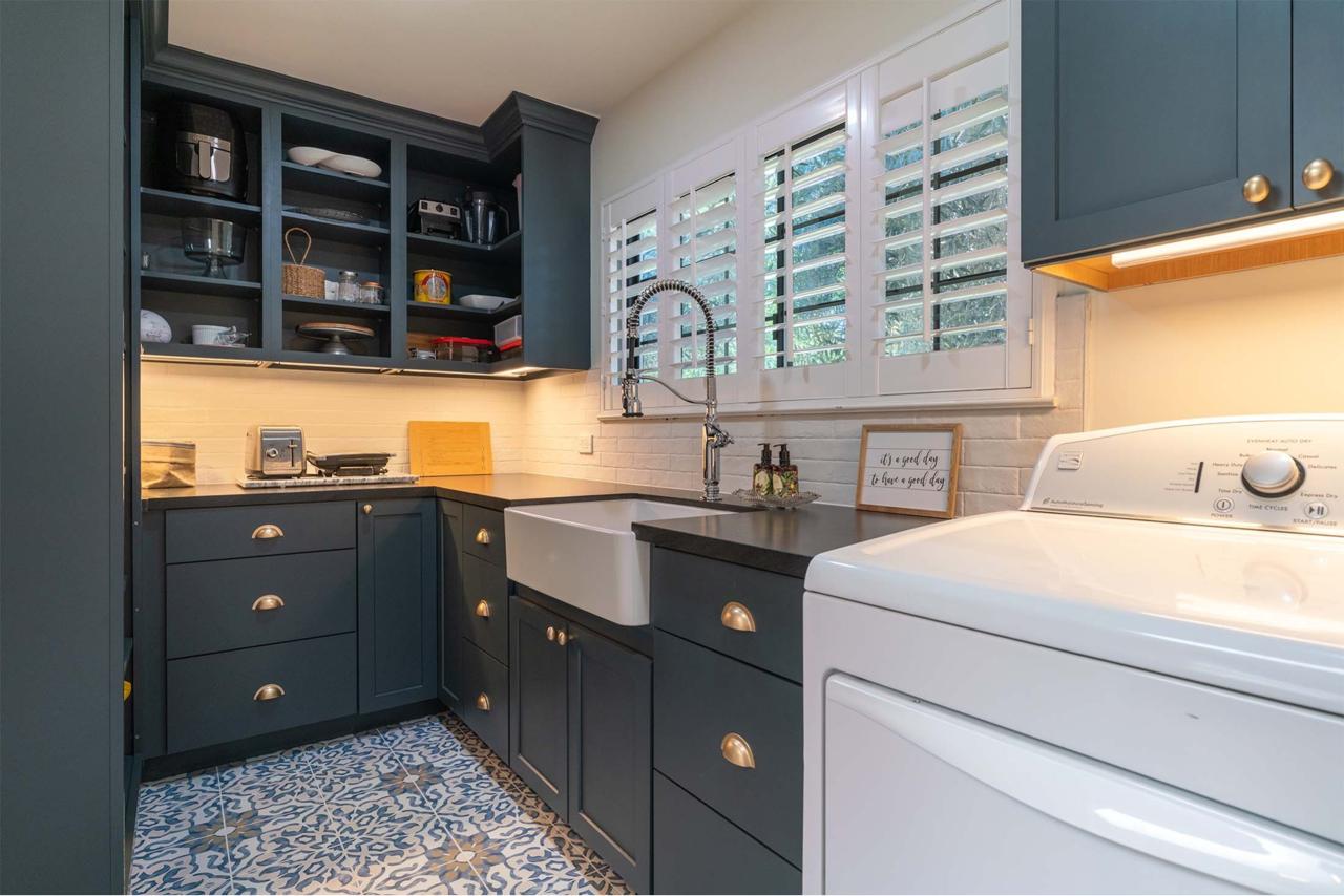 Stunning contemporary kitchen addition by professional contractors featuring navy shaker cabinets with gold hardware, white quartzite waterfall island, and modern glass-front upper cabinets.