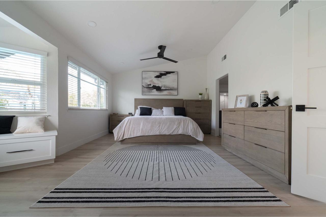 Spacious master bedroom from partial second story addition in Los Gatos featuring dramatic glass partition wall, modern ceiling fan, and open contemporary layout.